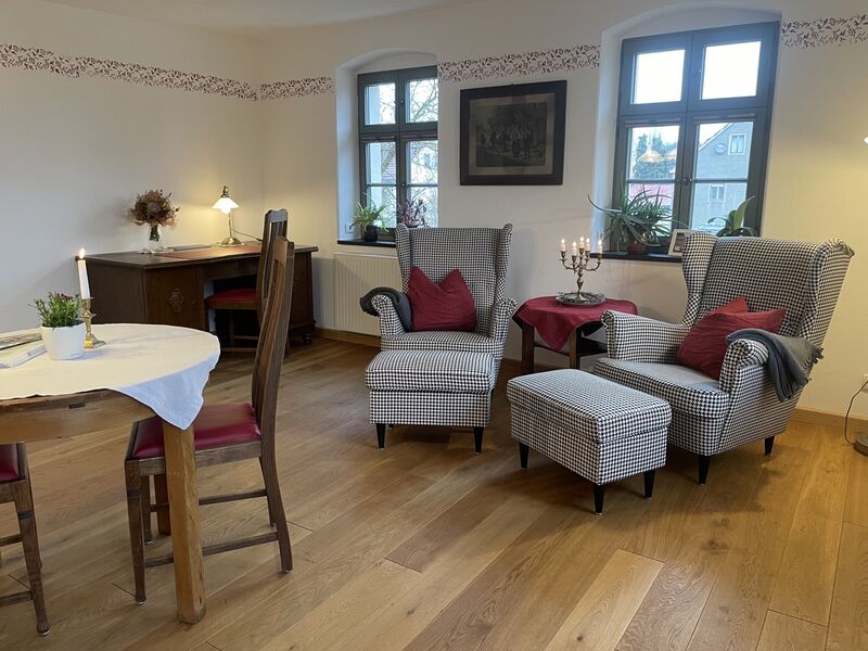 Im Wohnzimmer steht ein Esstisch mit Stühlen, zwei Ohrensessel, sowie ein Schreibtisch.